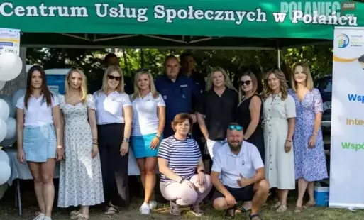 Zdjęcie przedstawia dużą grupę osób, składającą się z kobiet i mężczyzn, pozujących przed zielonym namiotem z napisem 'Centrum Usług Społecznych w Połańcu'. Wszyscy uśmiechają się do aparatu. Wśród nich jest kilku mężczyzn, w tym jeden w policyjnym mundur